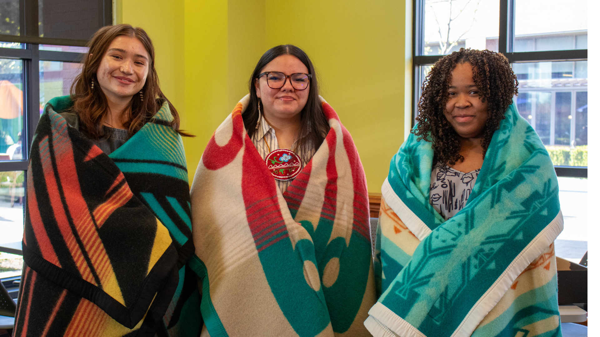 Three women with native blankets wrapped around each one 