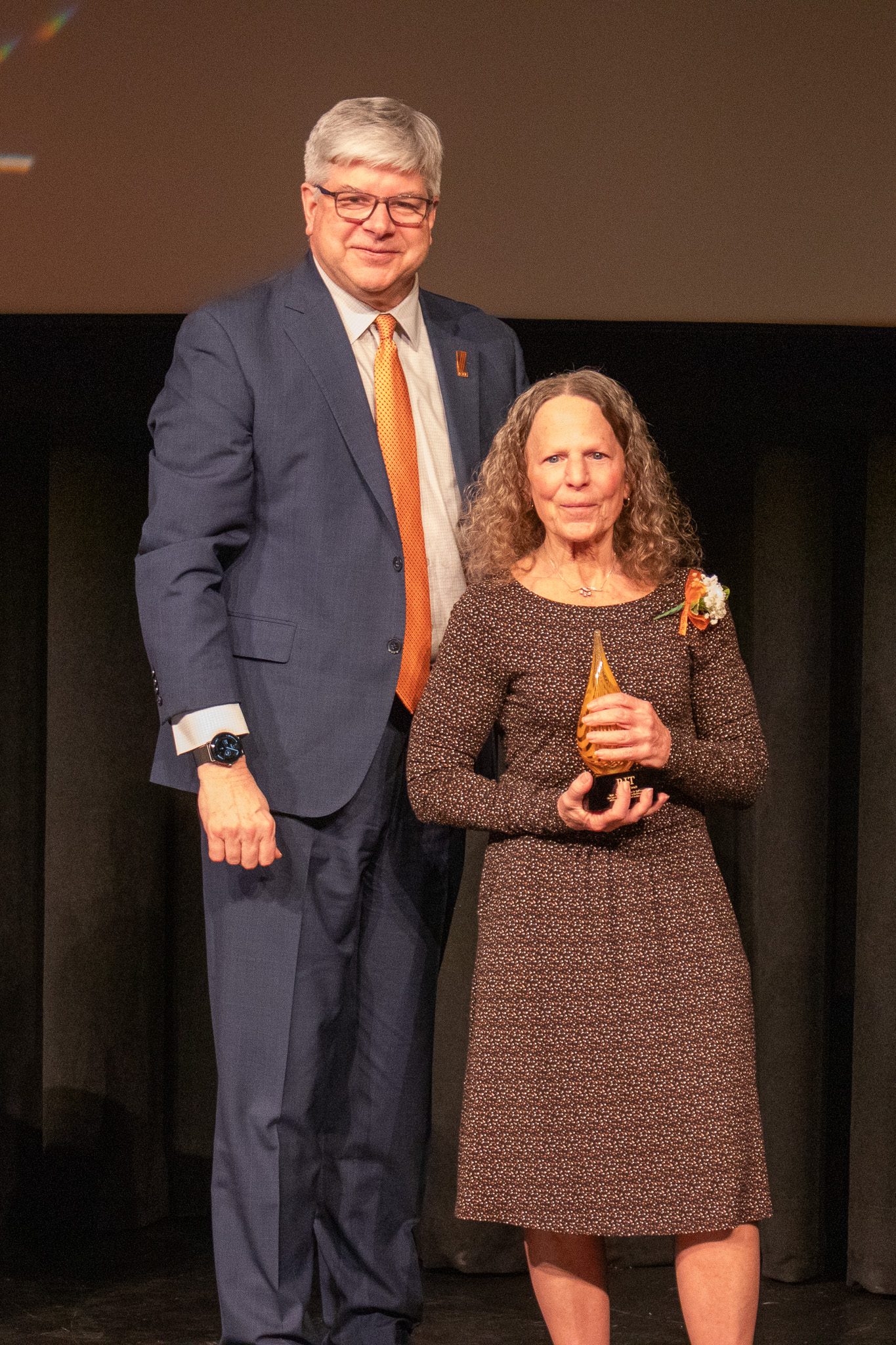 Photo of two people on stage, one is holding an award