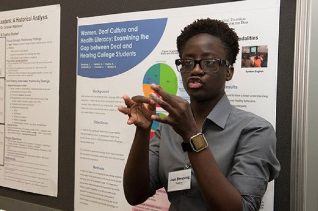 Student showcasing work in front of poster.