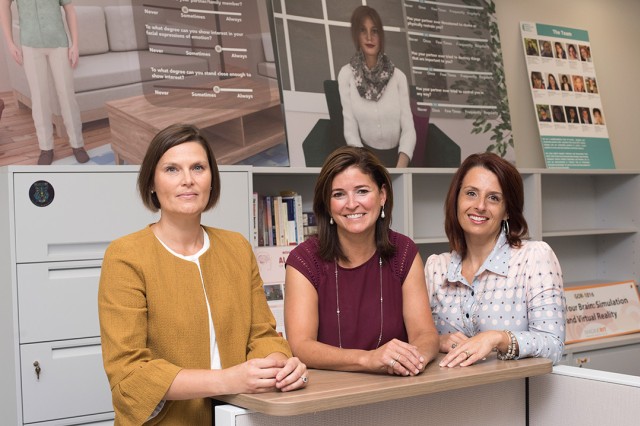 Three women stand and pose for a photo in an office setting.