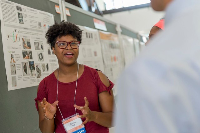 Cianna Dresden Hall excitedly explains her research to onlookers, talking with her hands and smiling as she speaks.