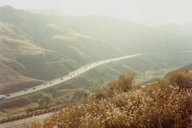 View of mountains with road cutting through and vehicles traveling on the road.