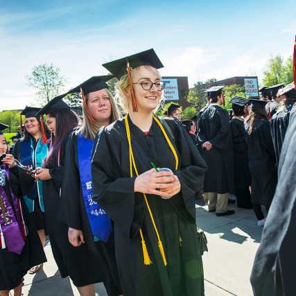 Group of students stands outside wearing black caps and gowns