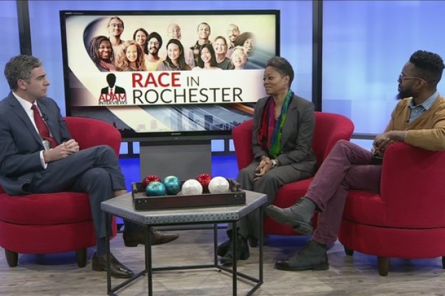 THree people sit in red chairs on set of TV news station