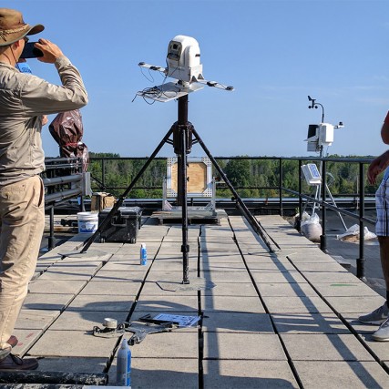 Three researcher watch hyperspectral camera on roof.