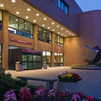 Outside of brick building with glass entryway and cube scultpure, taken at dusk.