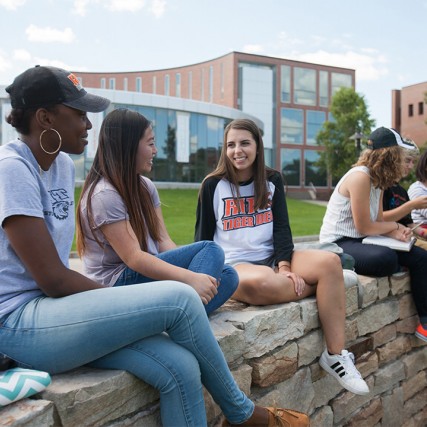 Six students sit on rock wall.