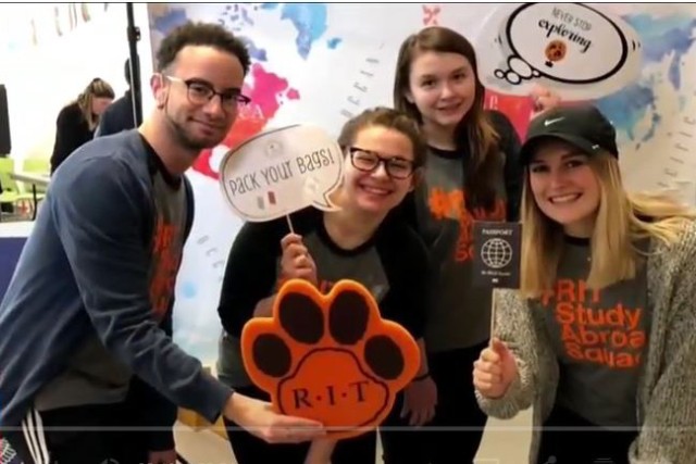 Students pose holding foam tiger paws and signs that read: "Pack your bags" and "Never stop exploring"