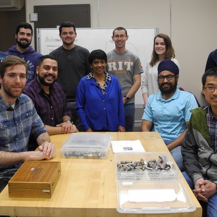 Group of students and researchers sit and stand around table.