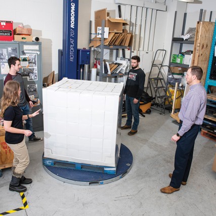 Students and professor stand around pallet with boxes.