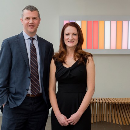Man in blue suit and woman in black dress stand next to each other.