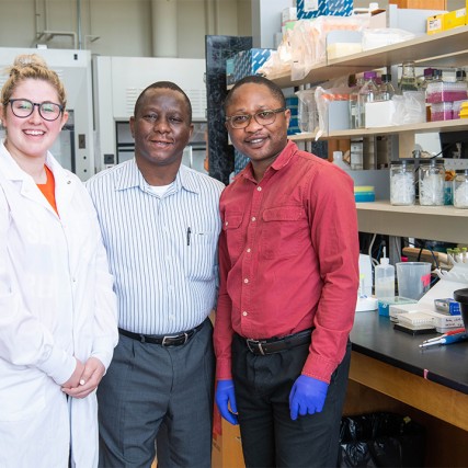 Three people smiling and standing in a lab