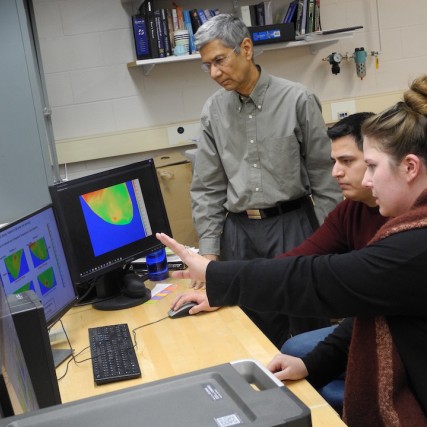Two students and a professor work on a computer with infrared imaging of cancerous tumors.