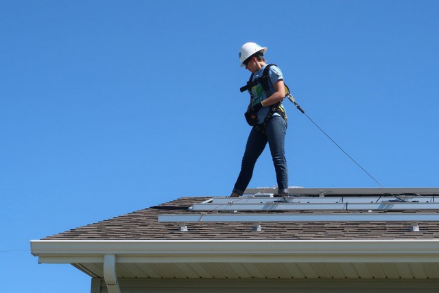 Worker wearing hardhat, harness and tether stands on roof.