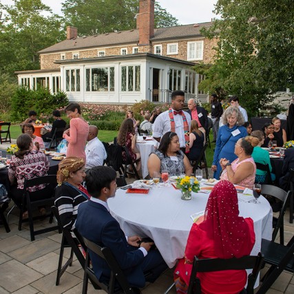 Groups of students and deans sitting at round tables on patio.
