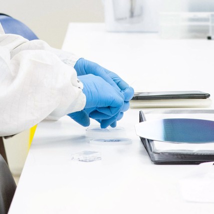 Gloved hands work on semiconductor wafer.
