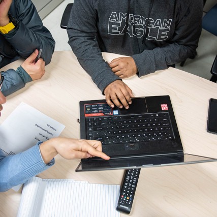 Overhead view of students and faculty member working on laptop.