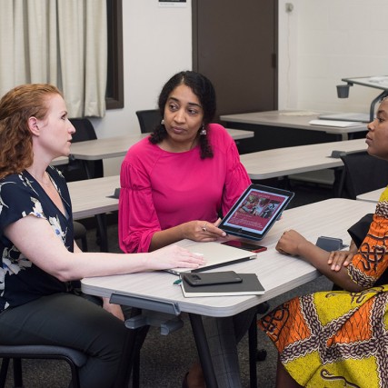 Three women discuss app on tablet.
