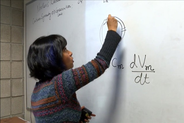 Professor writes equation on dry-erase board.