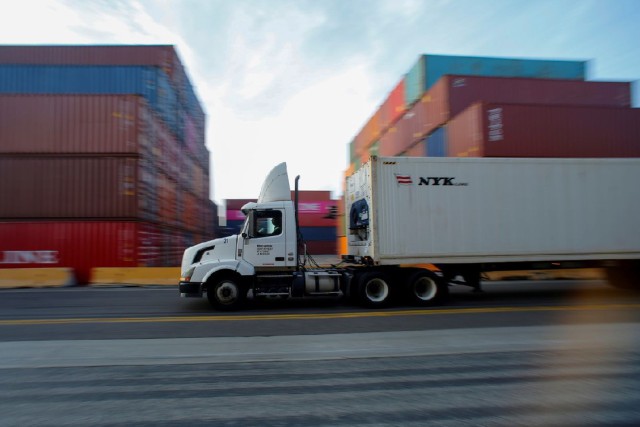 A semi truck carries its cargo through a shipment yard. 