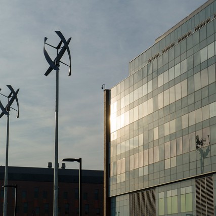 Three wind turbines in front of glass building.
