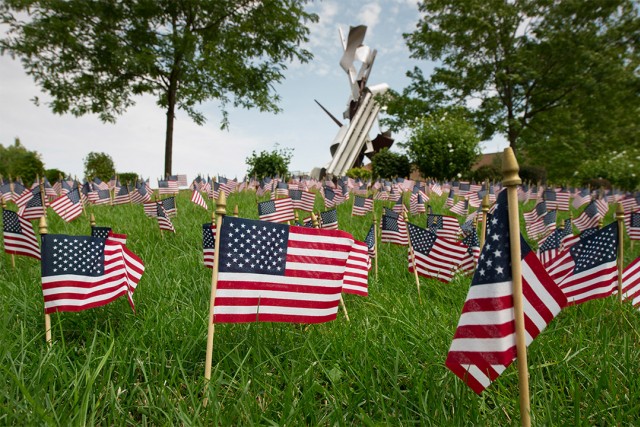 small American flags stuck into the lawn in front of a metal sculpture.