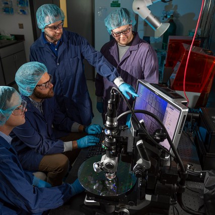 four researchers looking at computer that's analyzing a quantum photonics wafer.