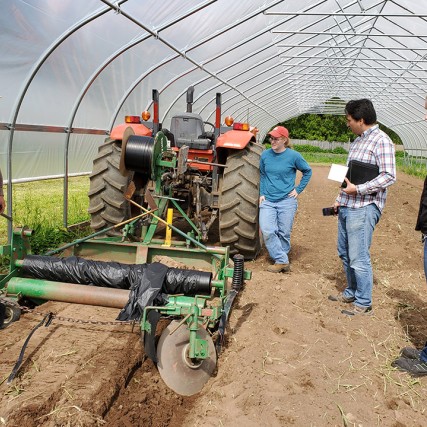 farmers and researchers in greenhouse using tractor to put down mulch barrier.