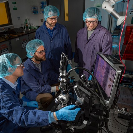 Four scientists analyzing quantum photonics wafer.