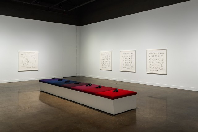 art exhibit of 7 headphones sitting on a bench with purple, blue, and red cushions.