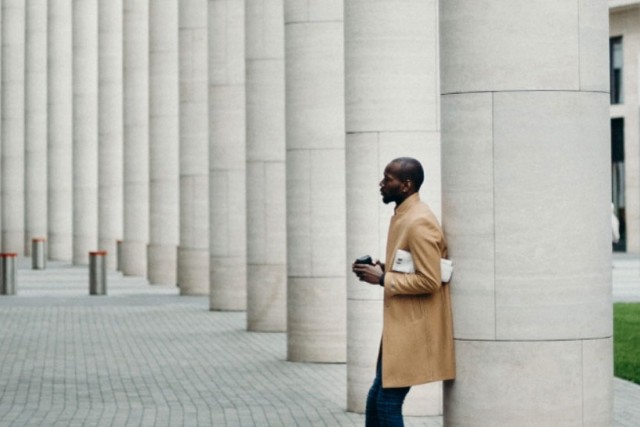 man leaning against stone column in outdoor plaza.