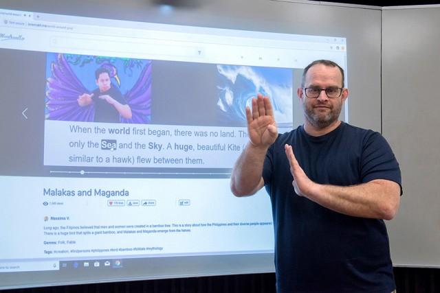 faculty member using sign language in front of a presentation.