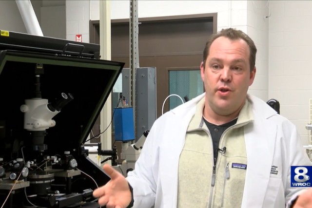 professor talking in front of microscope equipment.
