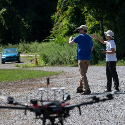 Two people walk next to a drone.