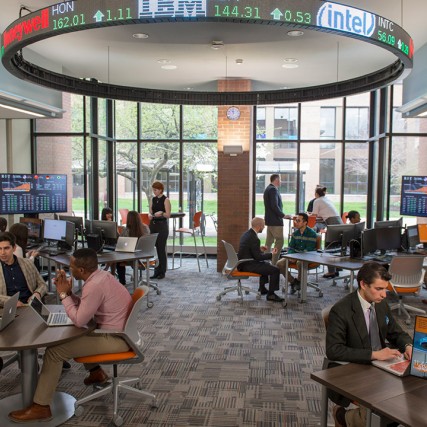students in a business lab with large, digital stock ticker.