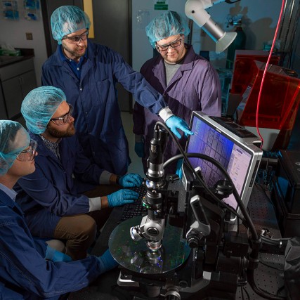 group of four scientists looking at a microchip.