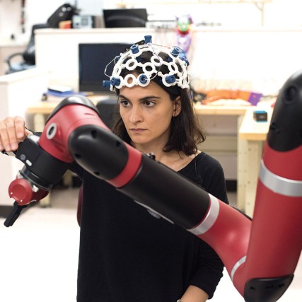 student wearing sensors on her head adjusts a robotic arm.