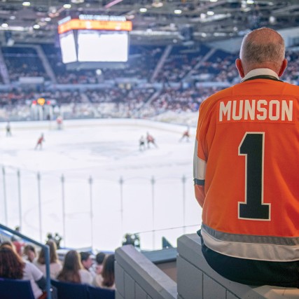 President Munson wearing a No. 1 jersey watches a hockey game in Blue Cross Arena.