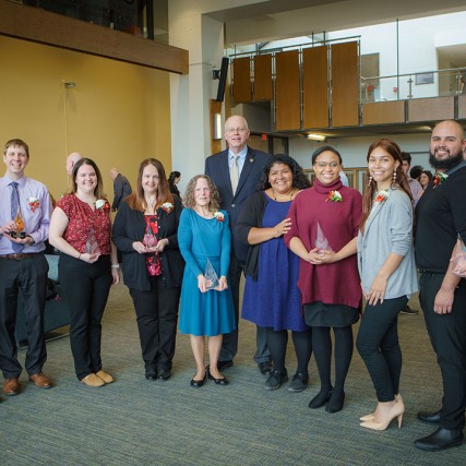 group of people standing in a semi-circle holding glass awards.