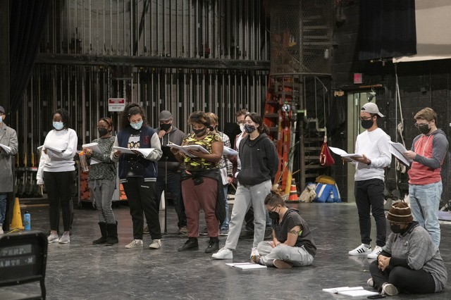 student actors standing and sitting on stage reading through a script.