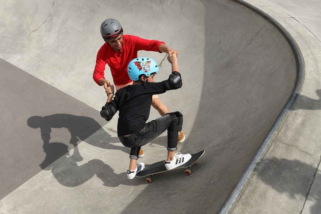 adult helping a kid to skateboard.