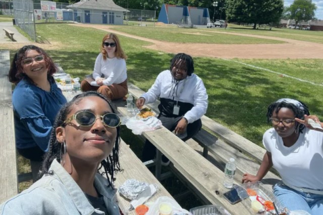 five people sitting on wooden bleachers eating food.
