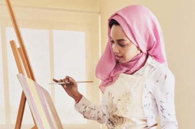 Zulfa Rasheed works on a painting that is leaning against an easel.