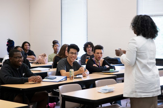professor lecturing to students seated at long tables.