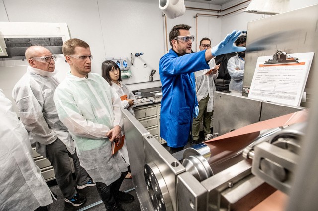 people wearing clean suits watching a demonstration of machinery.