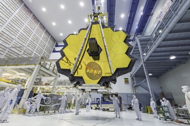 scientists in clean suits walking around the gold, hexagonal mirrors of the James Webb Space Telescope.