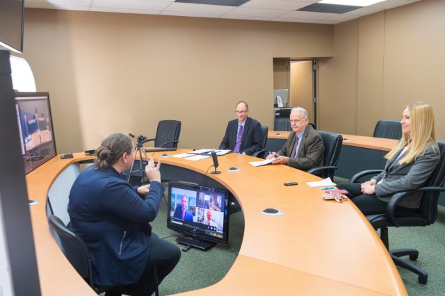 Image of NTID representatives at a table watching a large screen with EPA representatives. An interpreter sits between. 