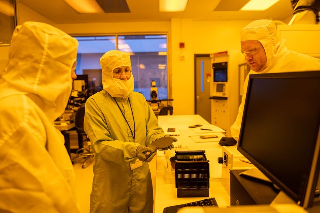 three people in clean suits looking at a computer chip.