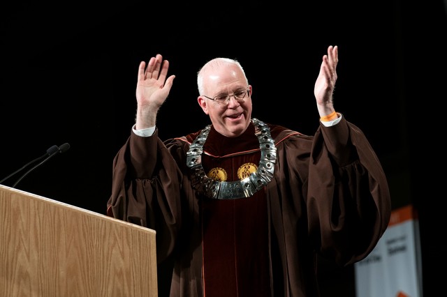 RIT President Munson wearing convocation ceremonial robes and holding his hands in the air.