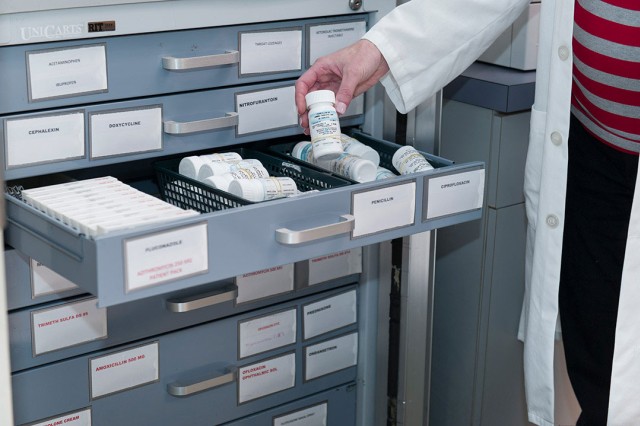 person holding a bottle of prescription medication from an open drawer of medicine boxes and bottles.